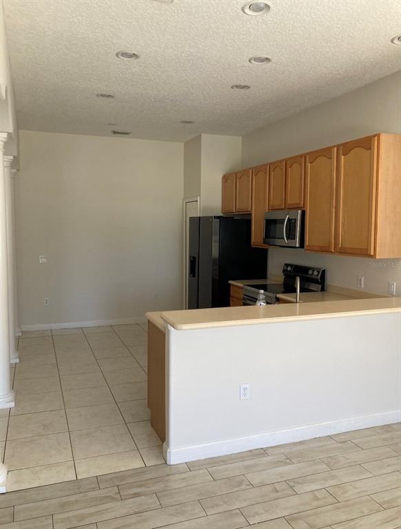 A kitchen features light wood cabinets, a black refrigerator, and a breakfast bar — 2102 BUNKER VIEW COURT, KISSIMMEE, FL