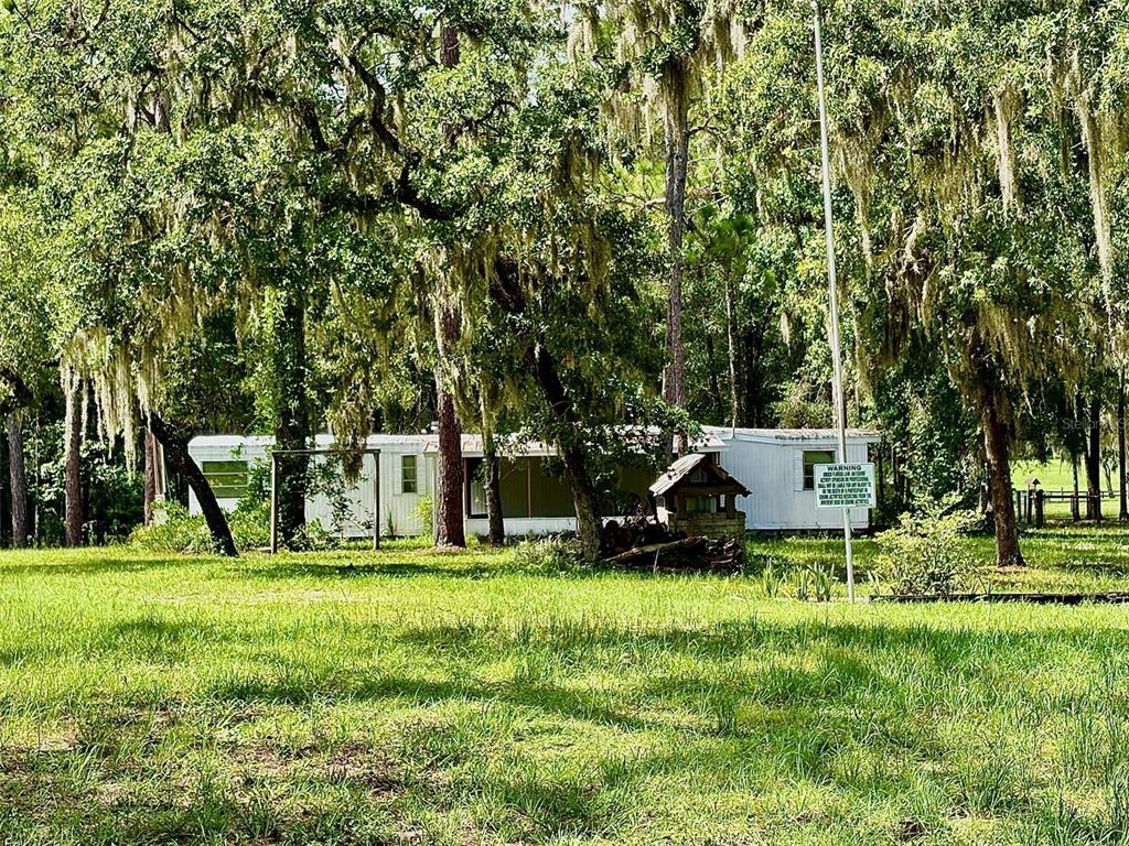 A white mobile home sits in a grassy yard surrounded by large, moss-covered oak trees — 10780 S FLUTTER TERRACE, INVERNESS, FL
