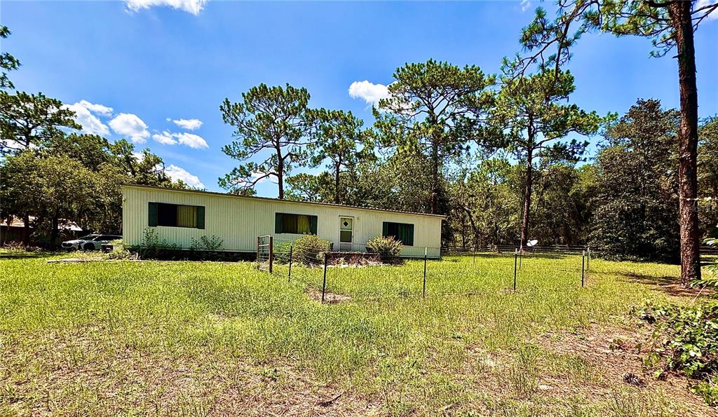 A single-story manufactured home sits in a grassy yard surrounded by tall pine trees — 10780 S FLUTTER TERRACE, INVERNESS, FL