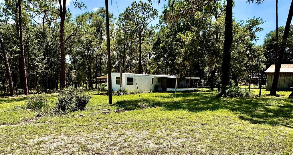 A white mobile home sits on a grassy lot surrounded by many tall trees — 10780 S FLUTTER TERRACE, INVERNESS, FL