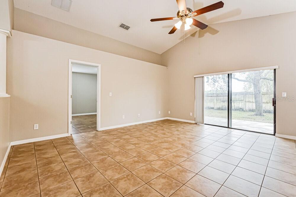 An empty room with tan tile flooring, vaulted ceilings, a ceiling fan, and sliding glass doors — 4222 BARNSLEY LANE, TAVARES, FL