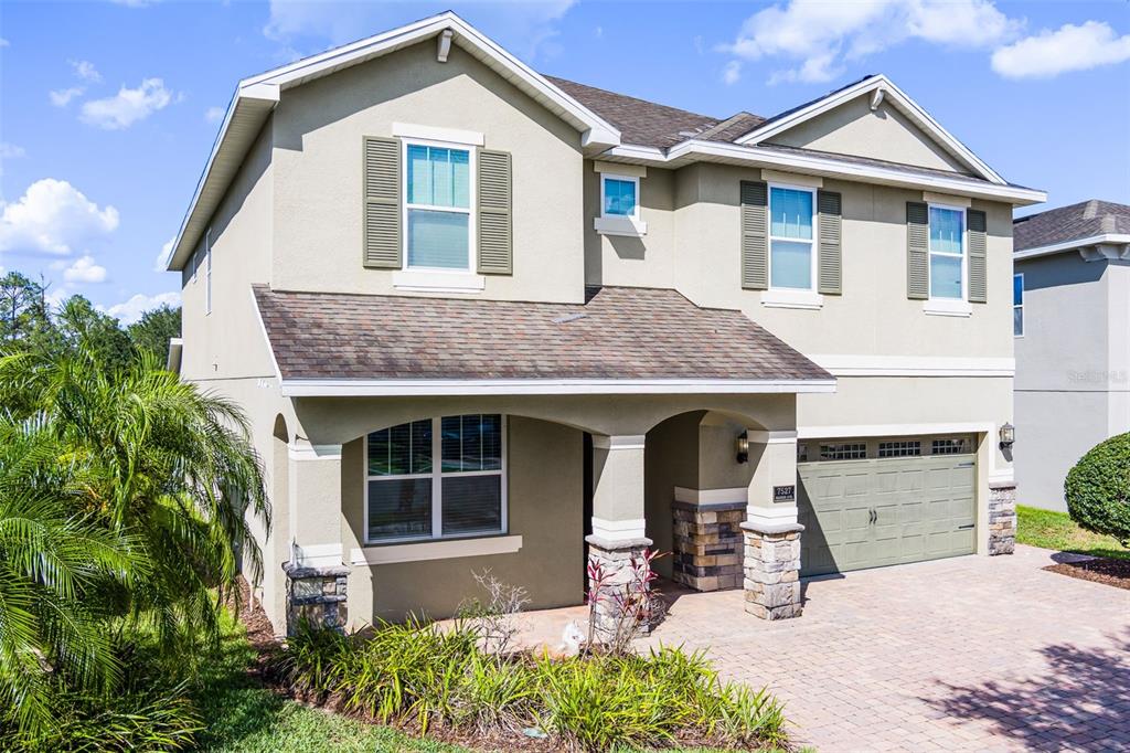 A two-story suburban house features a stone-accented porch, a paved driveway, and a garage — 7527 MARKER AVENUE, KISSIMMEE, FL