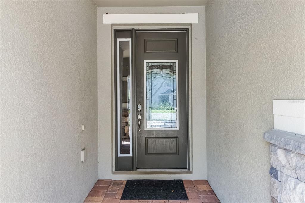 A dark brown front door with a glass insert and side light sits on a porch — 7527 MARKER AVENUE, KISSIMMEE, FL