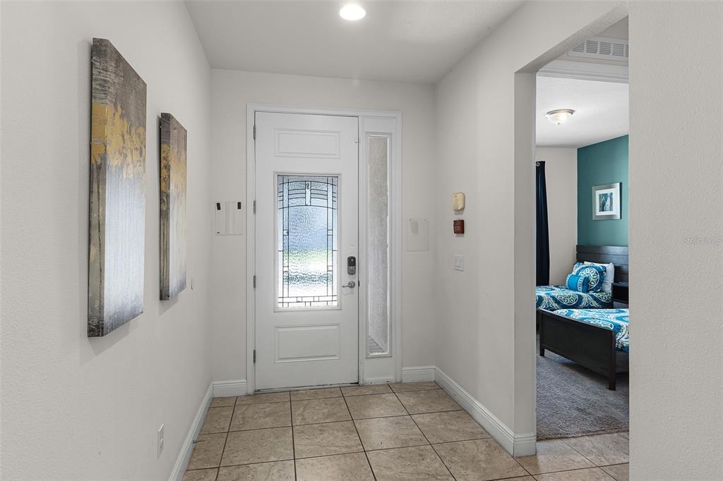 An entryway with tile flooring, a white front door, and a view into a bedroom — 7527 MARKER AVENUE, KISSIMMEE, FL
