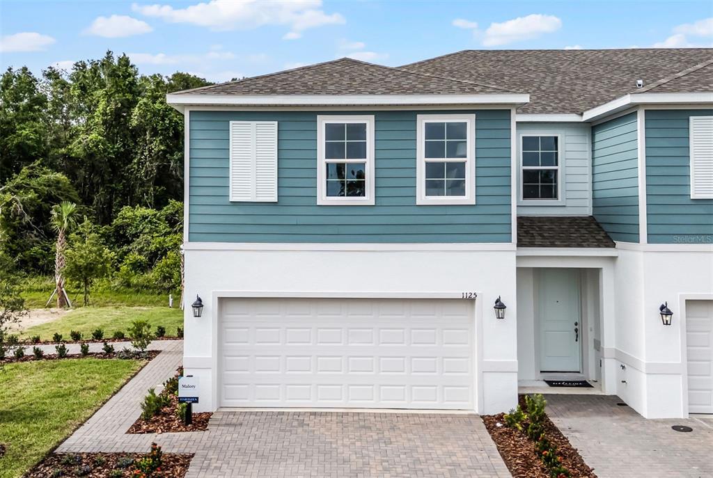 A two-story townhouse exterior features blue horizontal siding, white stucco, and a two-car garage — 1148 CYPRESS ELM DRIVE, DELAND, FL