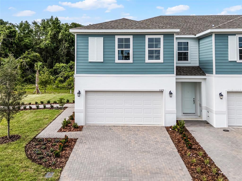 A two-story townhouse with blue siding, white stucco, a garage, and a paved driveway — 1148 CYPRESS ELM DRIVE, DELAND, FL