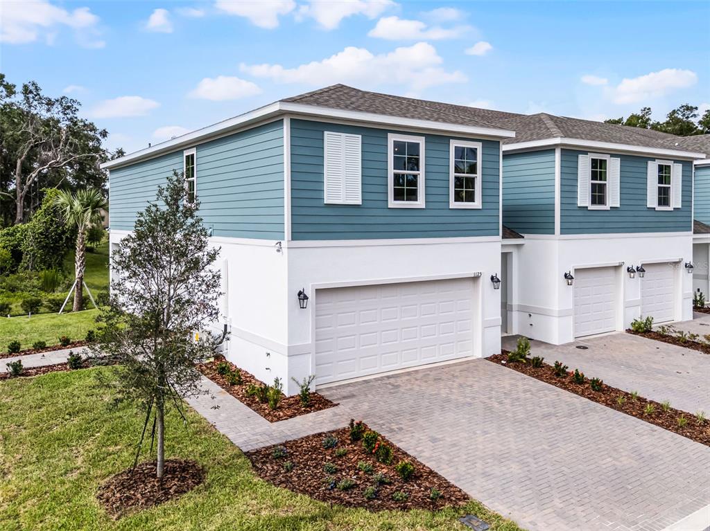 An exterior view of a two-story townhouse with blue siding, white stucco, and a garage — 1148 CYPRESS ELM DRIVE, DELAND, FL