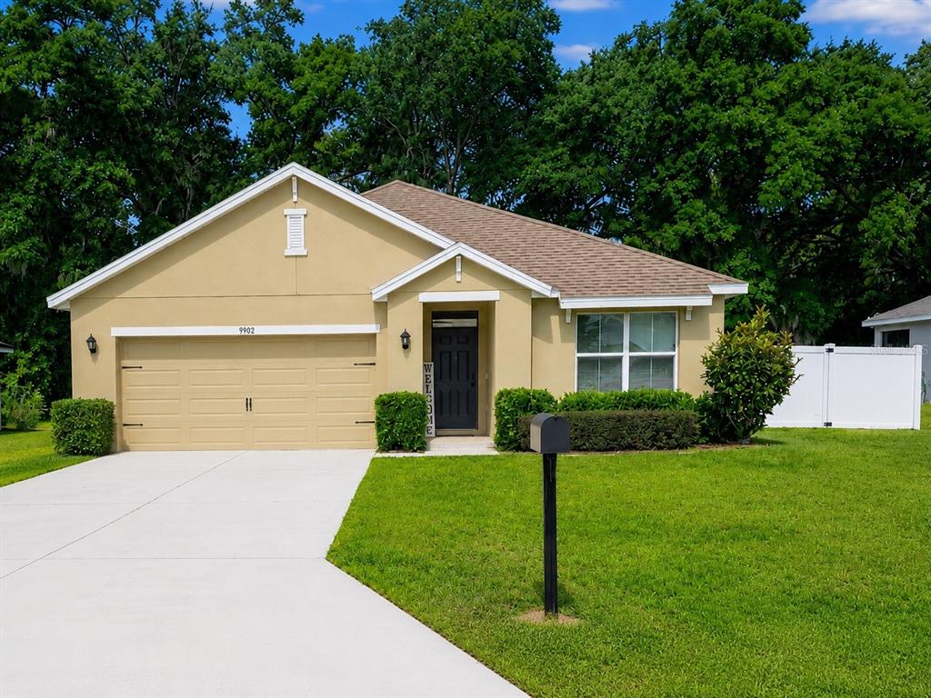 A single-story tan house with a two-car garage, front lawn, and a white fence — 9902 SE 37TH TERRACE, BELLEVIEW, FL