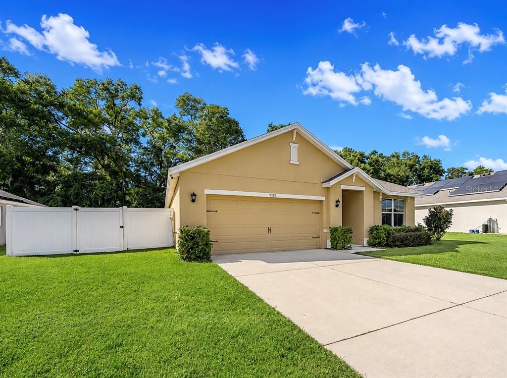 A tan single-story house with a two-car garage and a white vinyl fence — 9902 SE 37TH TERRACE, BELLEVIEW, FL
