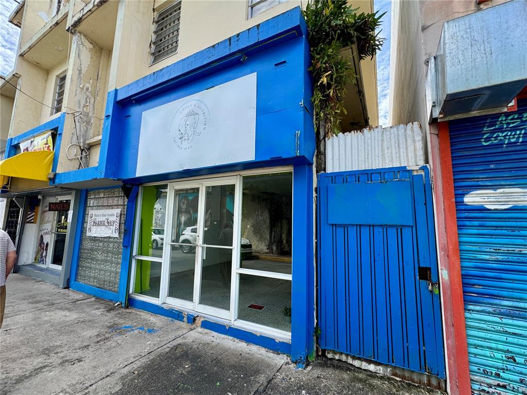 The exterior of a commercial building features a blue facade, glass storefront, and adjacent gate — 8 DR. VIDAL, HUMACAO, PR