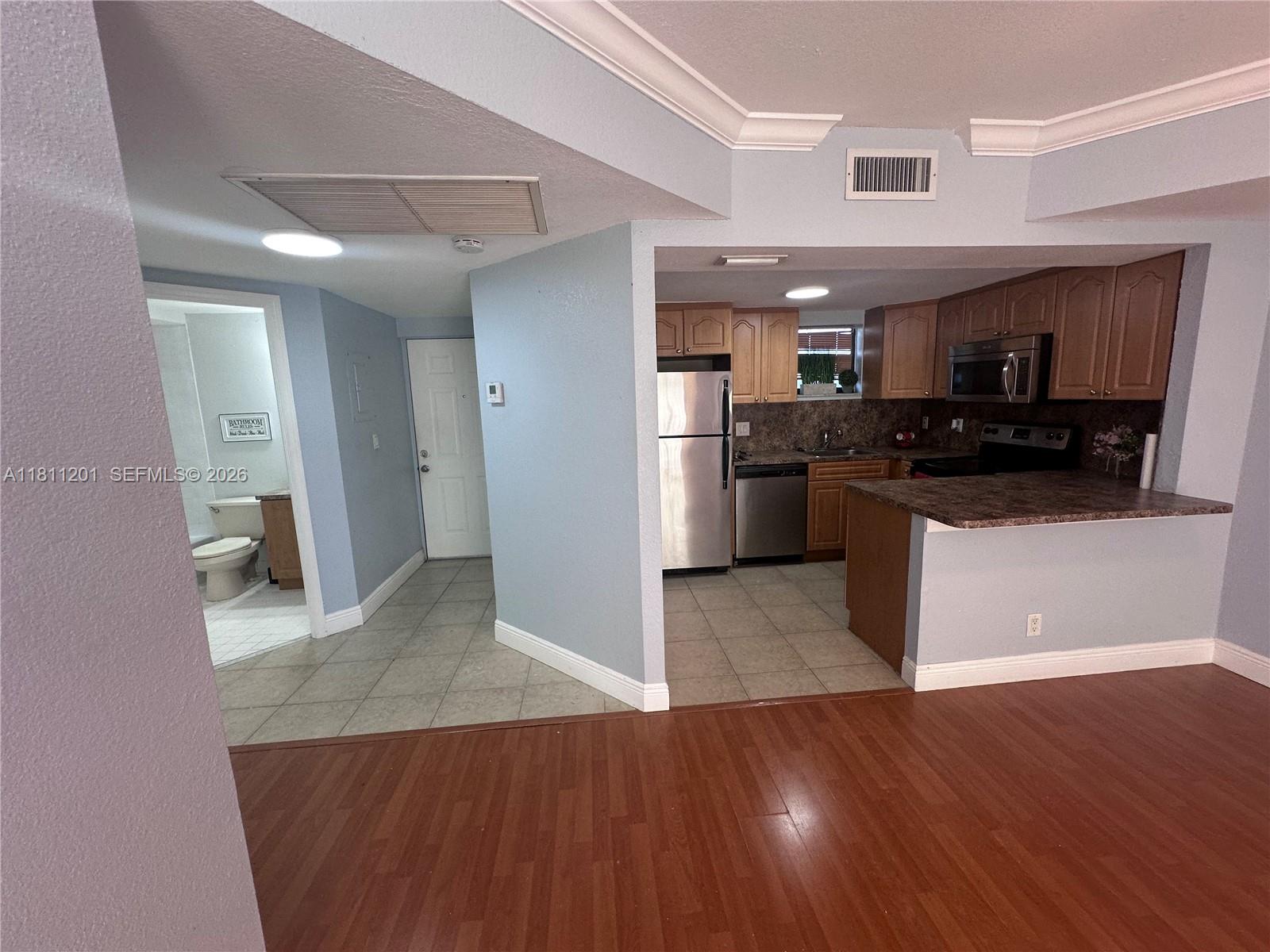 A kitchen with wood cabinets and stainless steel appliances sits beside a tiled entryway — 8290 Lake Dr # 502, Doral FL 33166, DORAL, FL