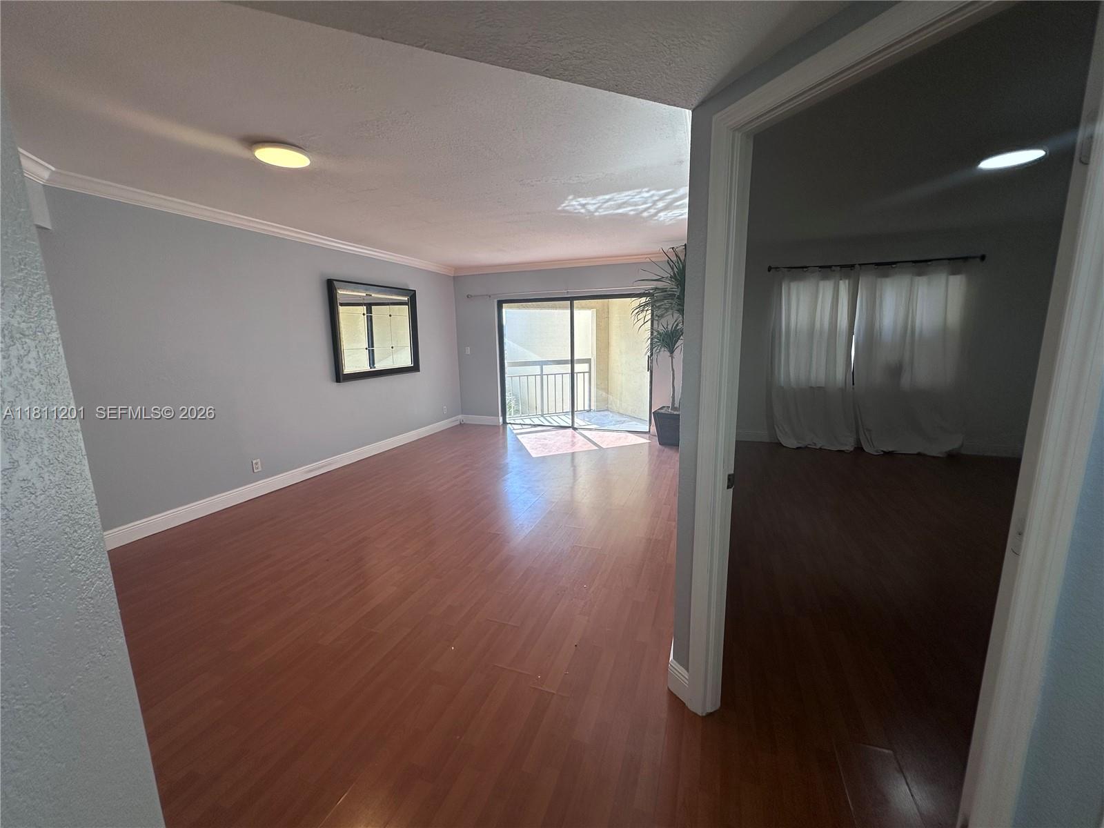 An empty living room with wood-look flooring leads to a balcony through sliding glass doors — 8290 Lake Dr # 502, Doral FL 33166, DORAL, FL
