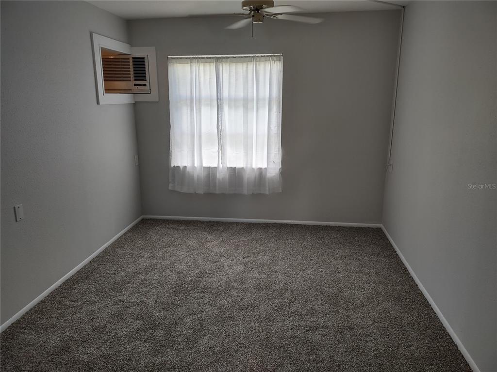A bedroom features gray walls, gray carpeting, a ceiling fan, and a window air conditioner — 1538 PLEASANT ROAD UNIT G34, BRADENTON, FL