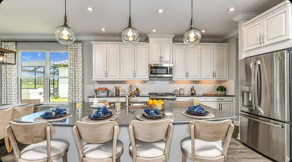 A kitchen features white cabinets, a large island with four chairs, and stainless steel appliances — 3826 MASANIELLO WAY, WESLEY CHAPEL, FL