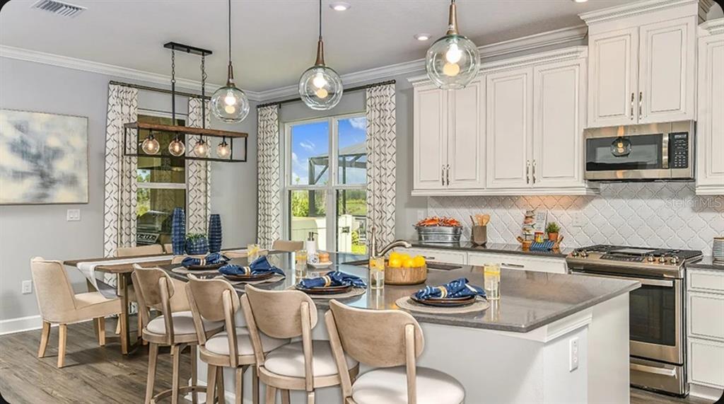 A kitchen with white cabinets, a large island, stainless steel appliances, and a dining area — 3826 MASANIELLO WAY, WESLEY CHAPEL, FL