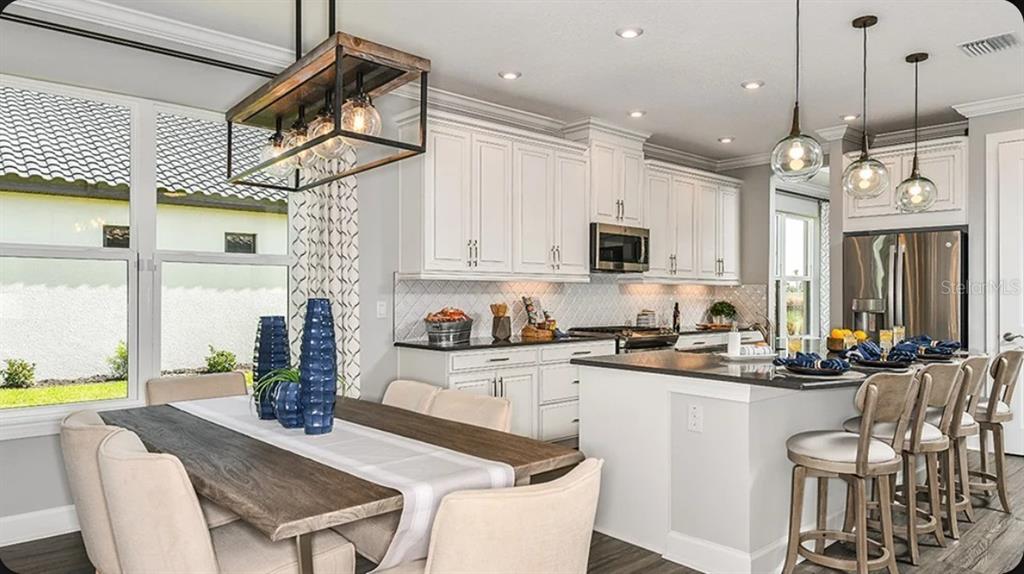 A kitchen with white cabinets and a dining area featuring a wooden table and chairs — 3826 MASANIELLO WAY, WESLEY CHAPEL, FL