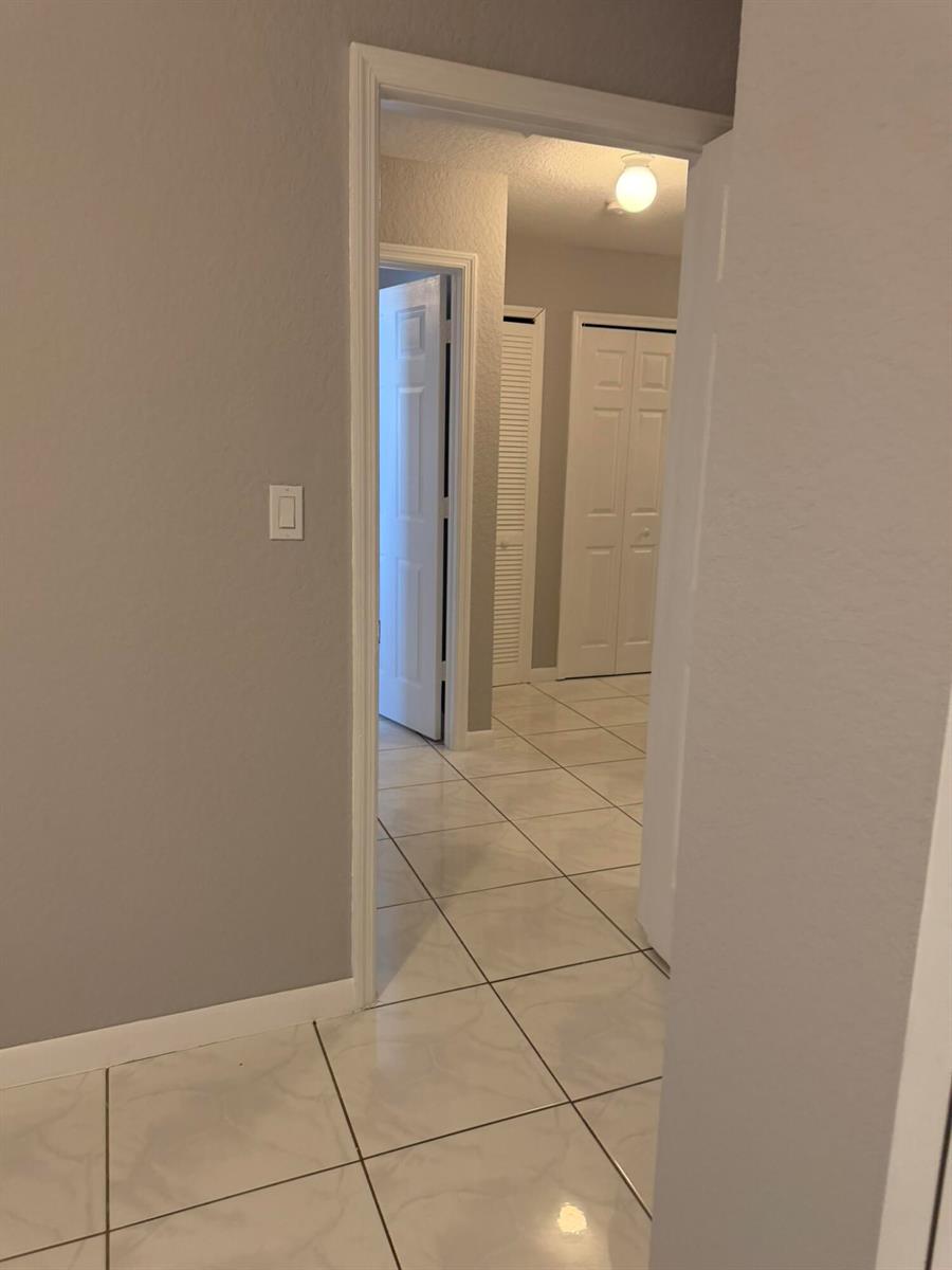 A hallway with light-colored tile flooring leads to a doorway and a closet — 663 S Biscayne River Drive, Miami FL 33169, MIAMI, FL