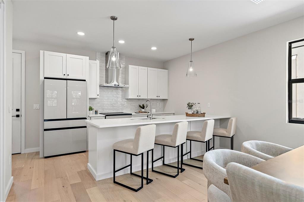 A modern kitchen features white cabinetry, a quartz island with bar stools, and light wood flooring — 423 11TH AVENUE S, ST PETERSBURG, FL