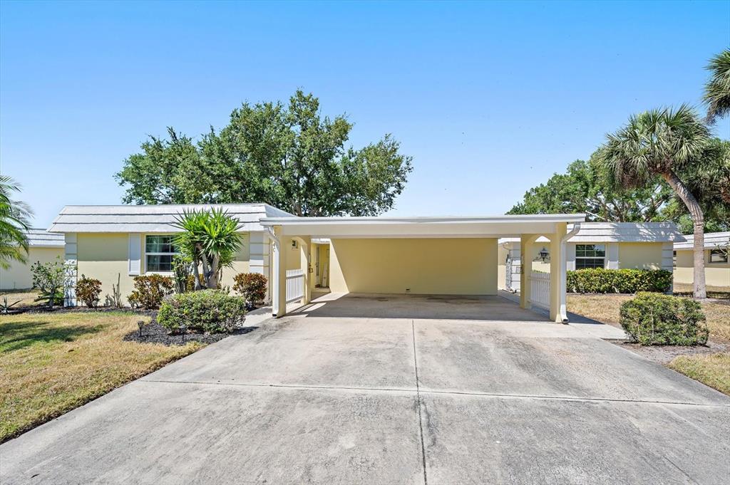 A yellow single-story house features a large attached carport and a concrete driveway — 5940 DRIFTWOOD AVENUE UNIT 15, SARASOTA, FL