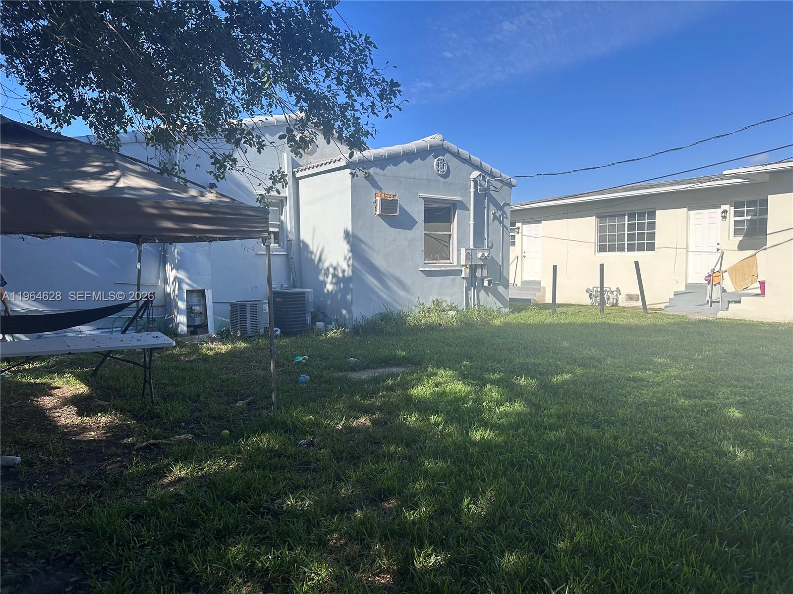 A grassy backyard features a blue house, a beige building, and a brown canopy tent — 2125 Bay Dr # C, Miami Beach FL 33141, MIAMI BEACH, FL