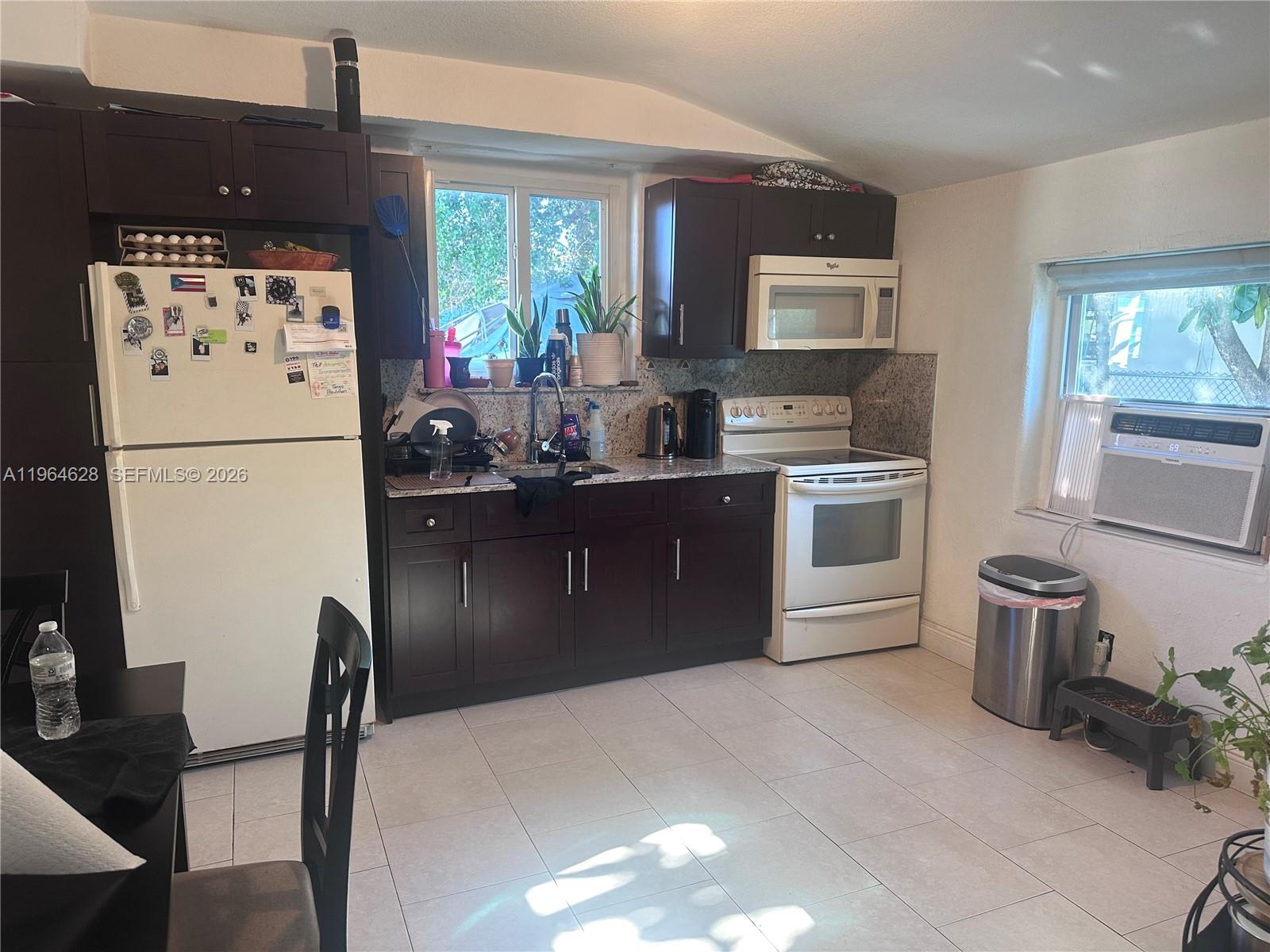 A kitchen features dark wood cabinets, granite countertops, white appliances, and light-colored floor tiles — 2125 Bay Dr # C, Miami Beach FL 33141, MIAMI BEACH, FL