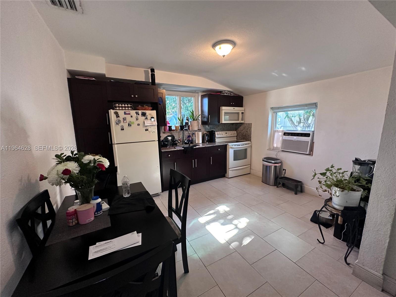 A kitchen features dark wood cabinets, white appliances, tile flooring, and a small dining table — 2125 Bay Dr # C, Miami Beach FL 33141, MIAMI BEACH, FL
