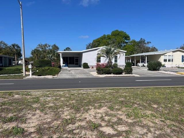 A light-colored manufactured home with a carport sits behind a paved road and sandy lot — 15025 BROOKRIDGE BOULEVARD, BROOKSVILLE, FL