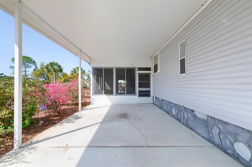 A concrete carport leads to a screened-in porch with light gray siding and stone skirting — 15025 BROOKRIDGE BOULEVARD, BROOKSVILLE, FL