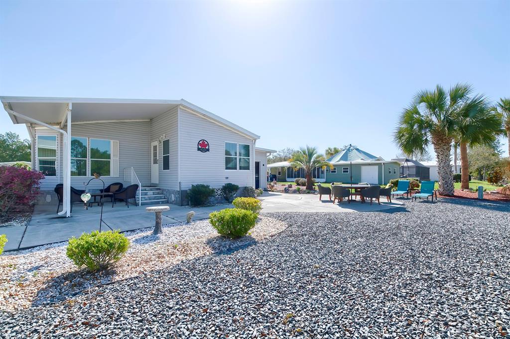 A light-colored mobile home with a covered patio, gravel yard, and outdoor seating area — 15025 BROOKRIDGE BOULEVARD, BROOKSVILLE, FL