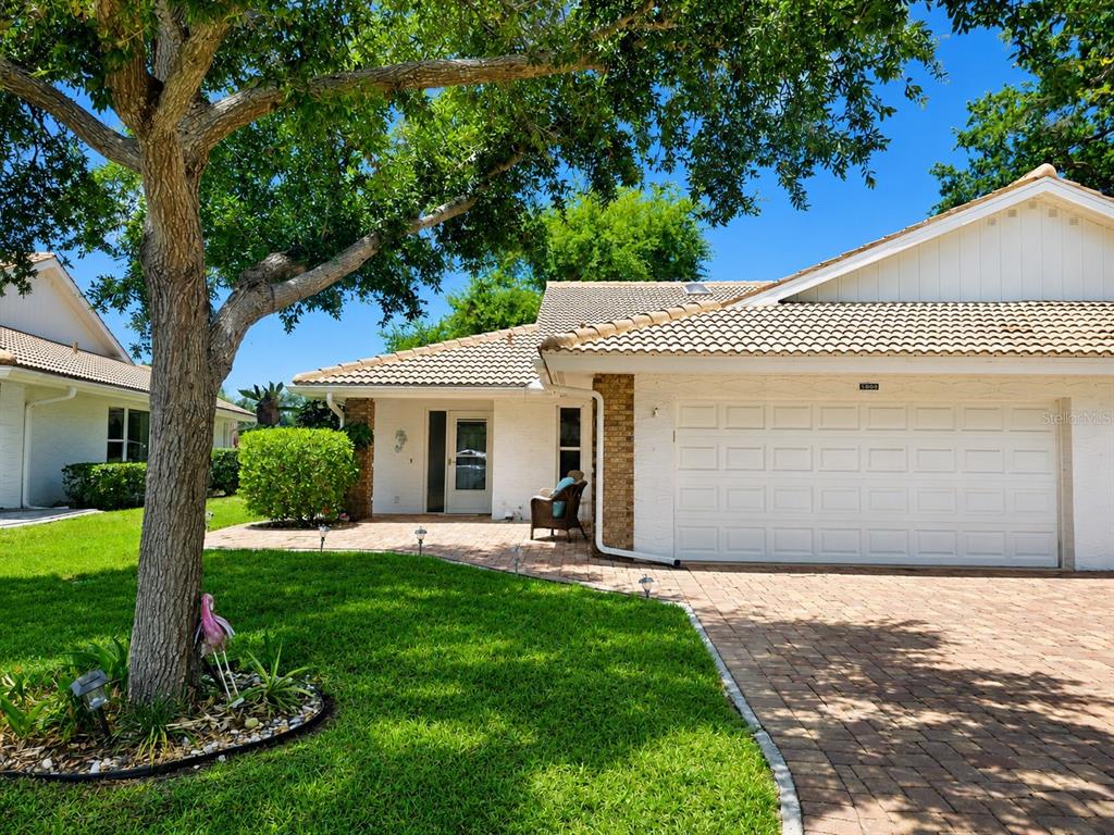 A single-story house with a white exterior, tiled roof, brick driveway, and a large tree — 5808 GARDEN LAKES DRIVE, BRADENTON, FL