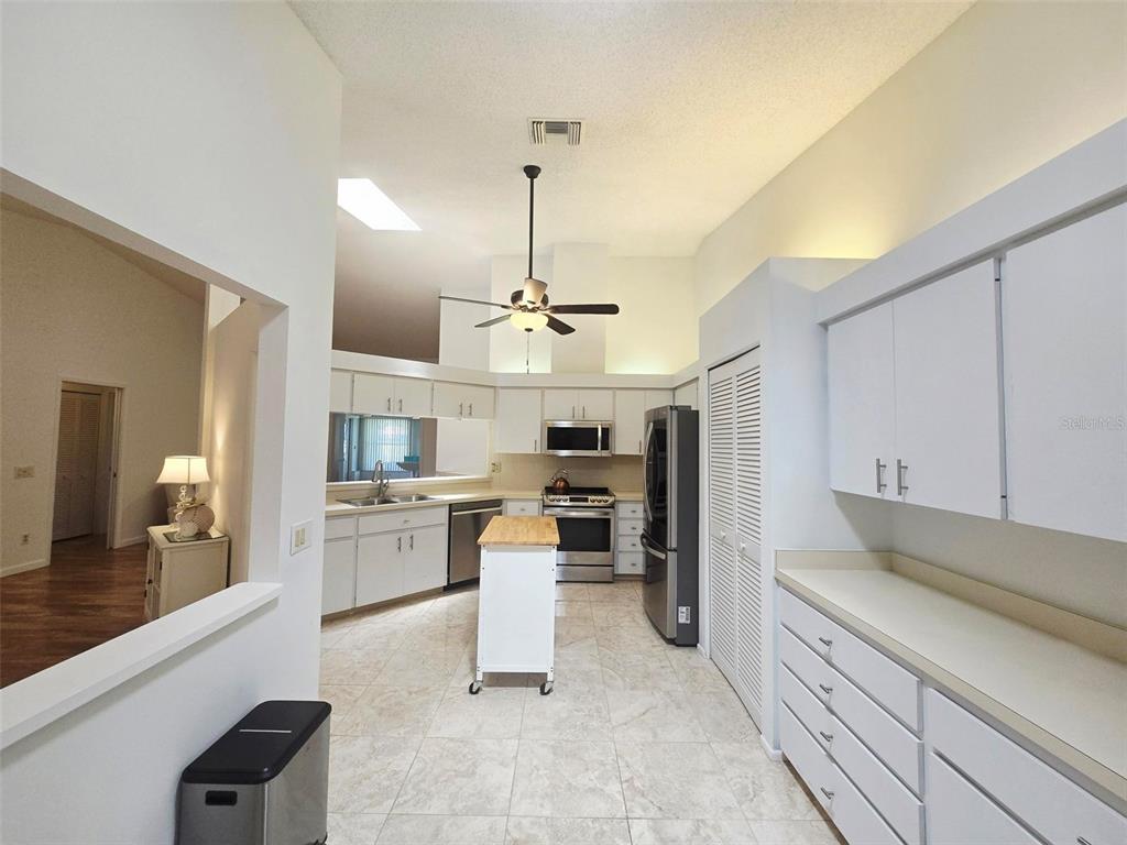 A kitchen with white cabinets, stainless steel appliances, a rolling island, and tile flooring — 5808 GARDEN LAKES DRIVE, BRADENTON, FL