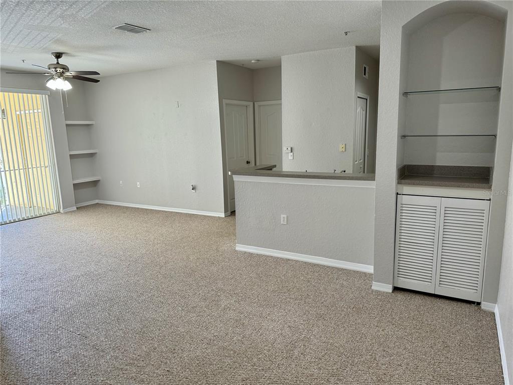 A carpeted living room features a ceiling fan, built-in shelving, and a sliding glass door — 1475 LAKE SHADOW CIRCLE UNIT 6105, MAITLAND, FL