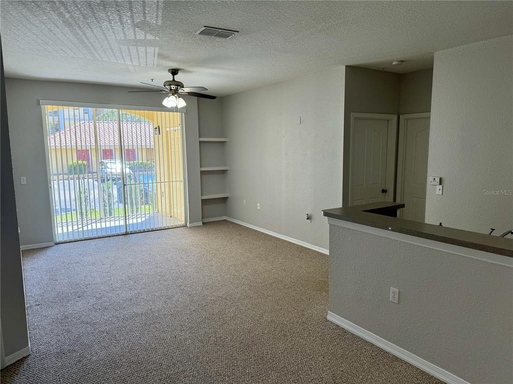 A carpeted living room features a ceiling fan, built-in shelving, and a sliding glass door — 1475 LAKE SHADOW CIRCLE UNIT 6105, MAITLAND, FL