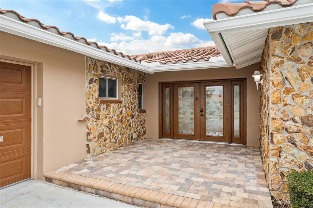 A stone-accented home exterior features a paver entryway and double glass-paneled front doors — 3734 TOPSAIL TRAIL, NEW PORT RICHEY, FL