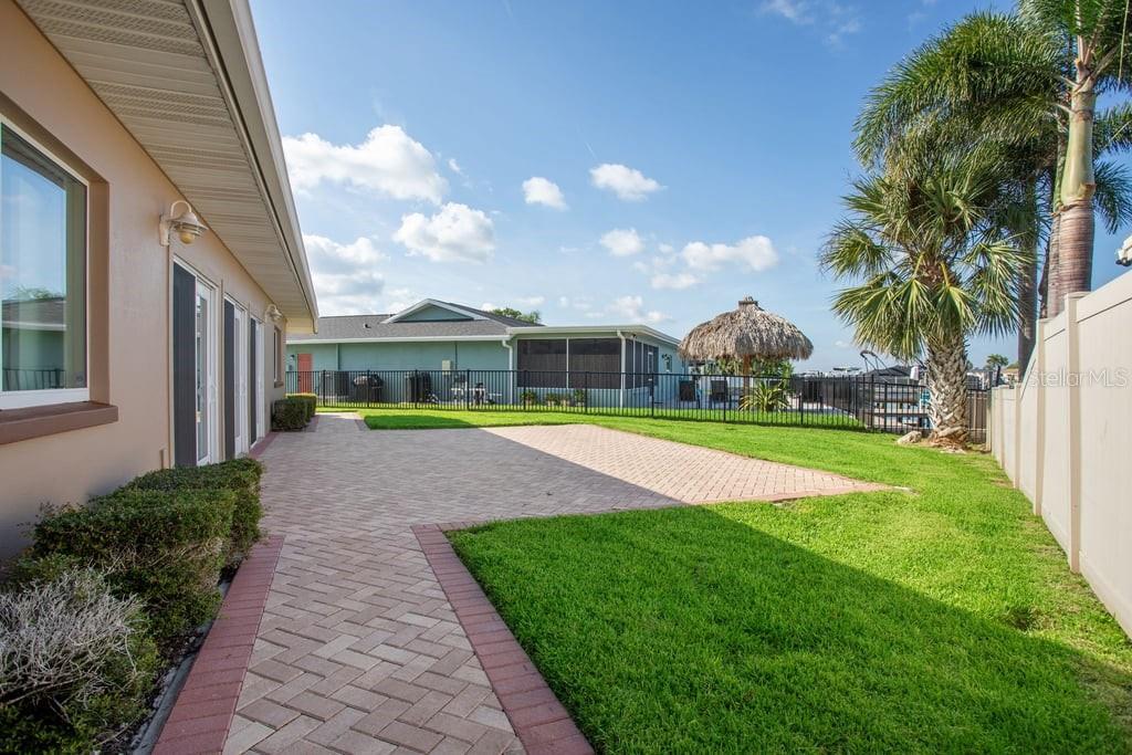 A paved patio area sits beside a house with a lawn and a palm tree — 3734 TOPSAIL TRAIL, NEW PORT RICHEY, FL