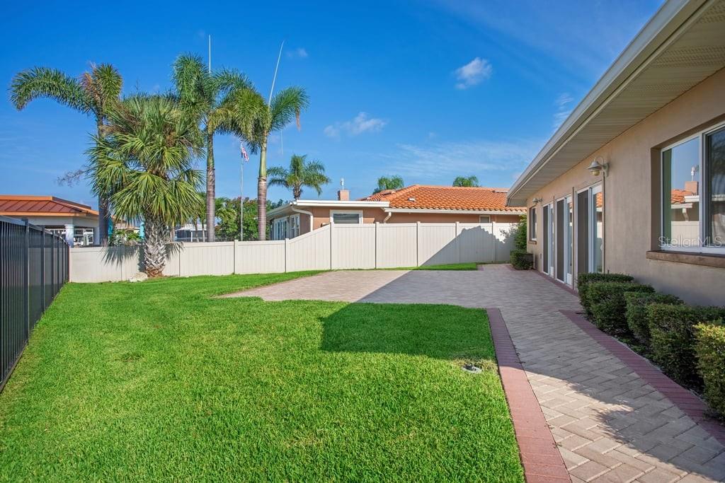 A backyard with a green lawn, a paved patio, and a white vinyl privacy fence — 3734 TOPSAIL TRAIL, NEW PORT RICHEY, FL