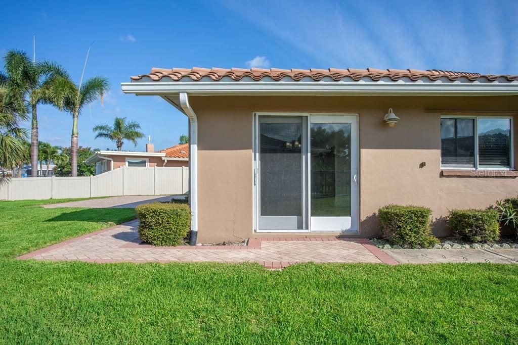 A tan house exterior features a sliding glass door, a brick patio, and palm trees — 3734 TOPSAIL TRAIL, NEW PORT RICHEY, FL