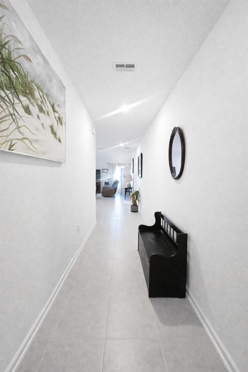 A hallway with light tile flooring, white walls, a black bench, and wall art — 1681 Teagan Lane, Winter Haven FL 33884, WINTER HAVEN, FL