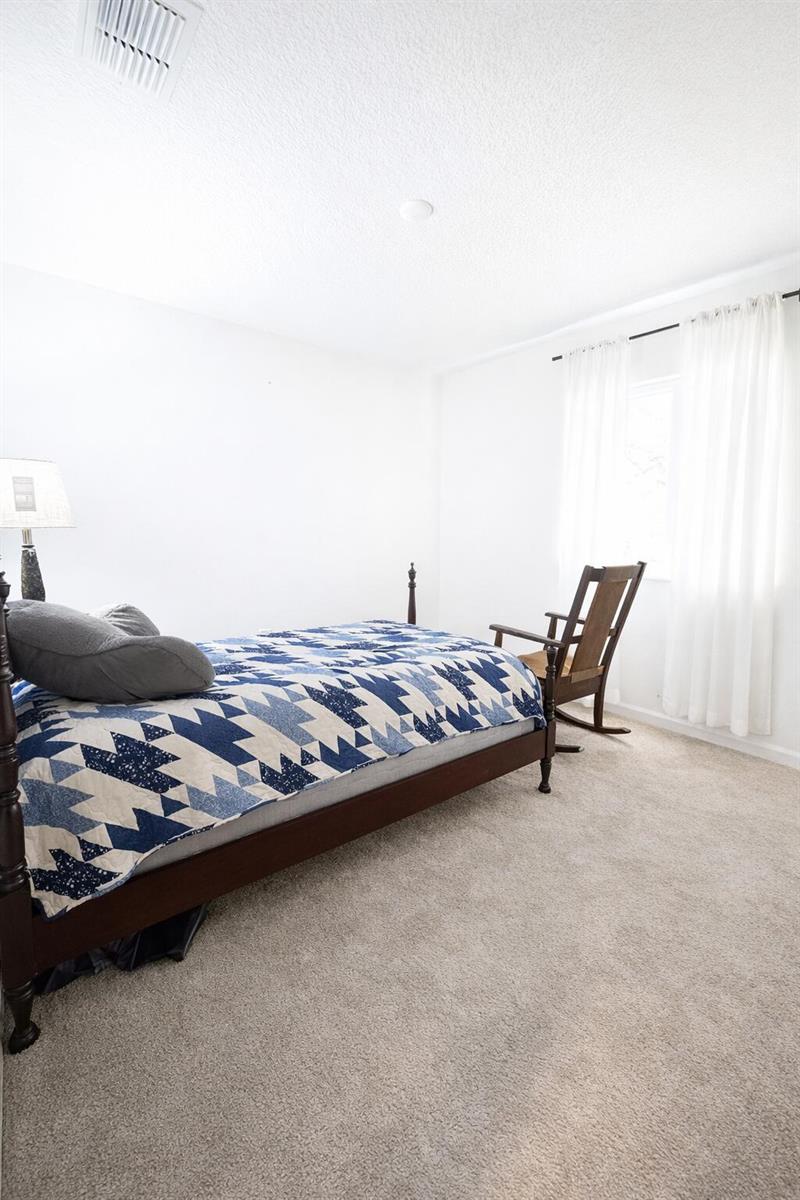 A bedroom features a dark wood bed with a blue patterned quilt and a rocking chair — 1681 Teagan Lane, Winter Haven FL 33884, WINTER HAVEN, FL
