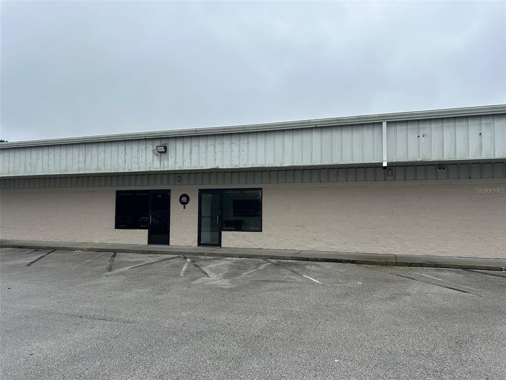 A single-story commercial building with a beige exterior, two glass entry doors, and asphalt parking — 11601 S ORANGE BLOSSOM TRAIL UNIT 205, ORLANDO, FL