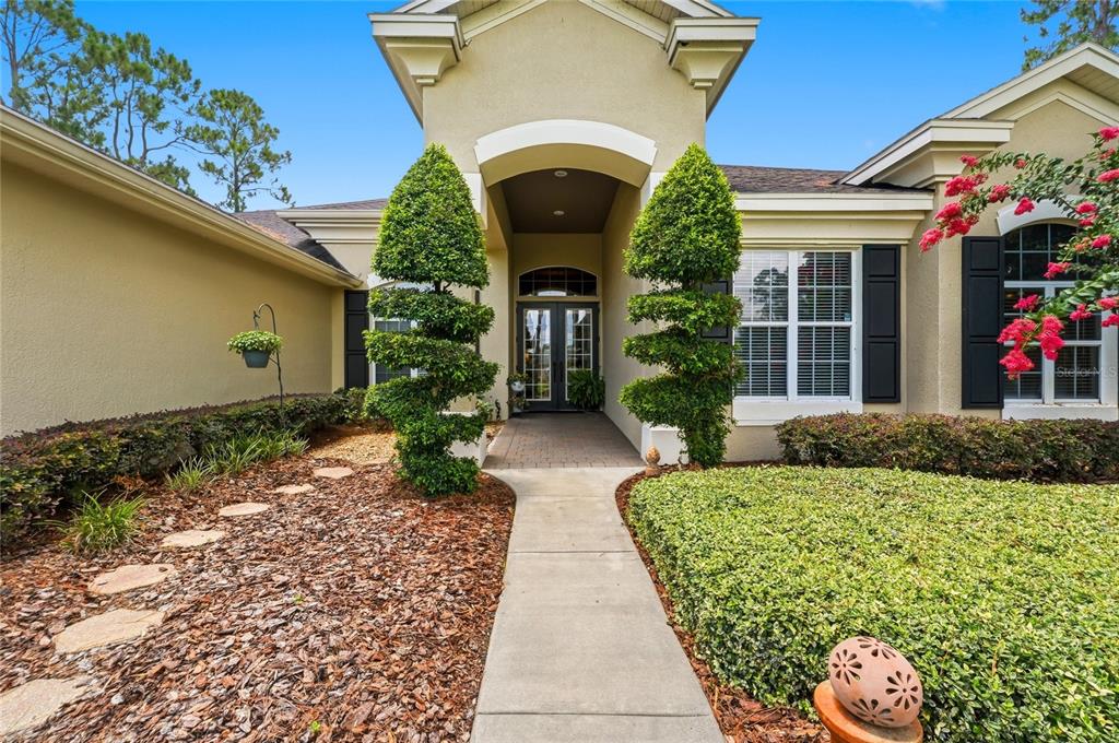 A concrete walkway leads to the front entrance of a house with two spiral-shaped topiaries — 140 SYLVANA COURT, AUBURNDALE, FL