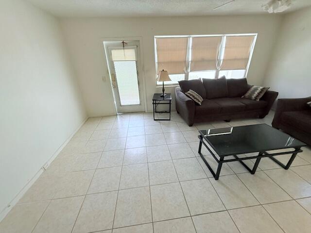 A living room with light tile flooring, a dark sofa, and a glass coffee table — 128 Upminster F Crescent, Deerfield Beach FL 33442, DEERFIELD BEACH, FL
