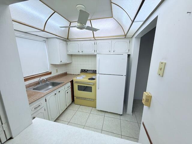 A kitchen features white cabinets, a yellow stove, a white refrigerator, and a tiled floor — 128 Upminster F Crescent, Deerfield Beach FL 33442, DEERFIELD BEACH, FL