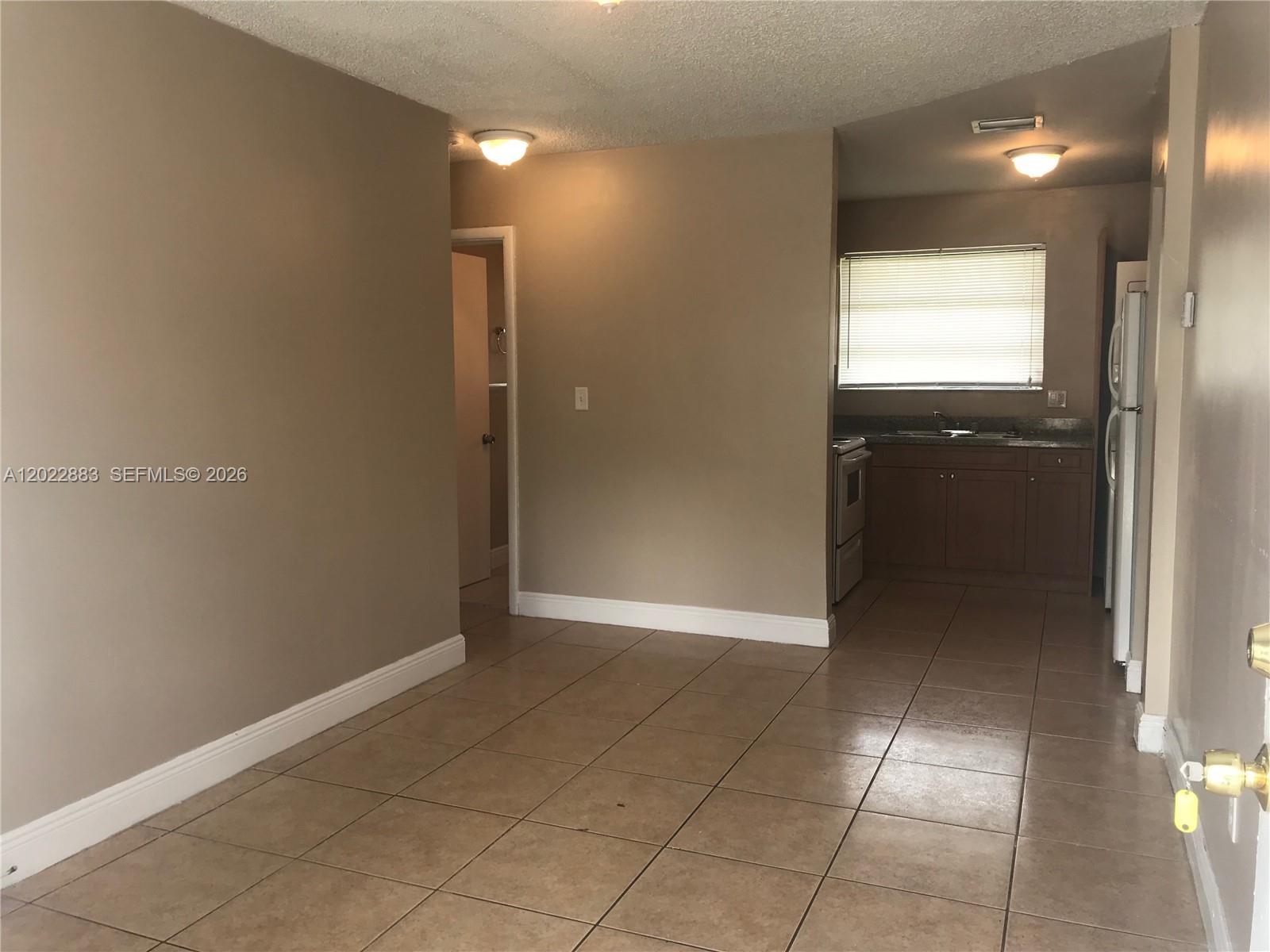 A room with tan tile flooring leads to a kitchen area with brown cabinets — 13315 Alexandria Dr # 3, Opa-Locka FL 33054, OPA-LOCKA, FL