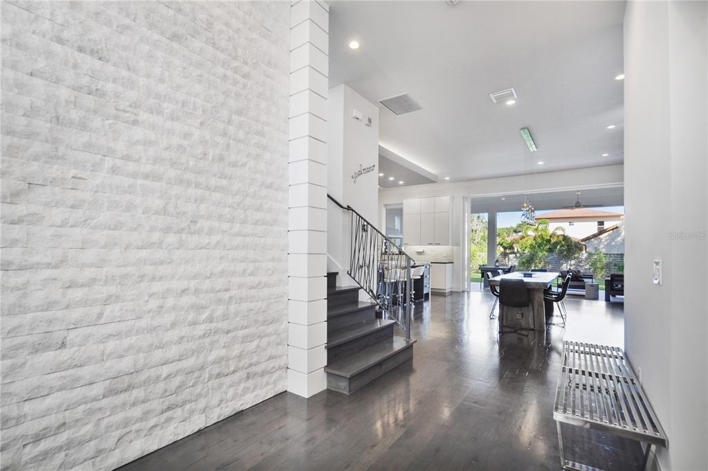 A modern interior features a white stone accent wall, dark wood stairs, and open-concept living — 1130 MECHANIC STREET, MAITLAND, FL