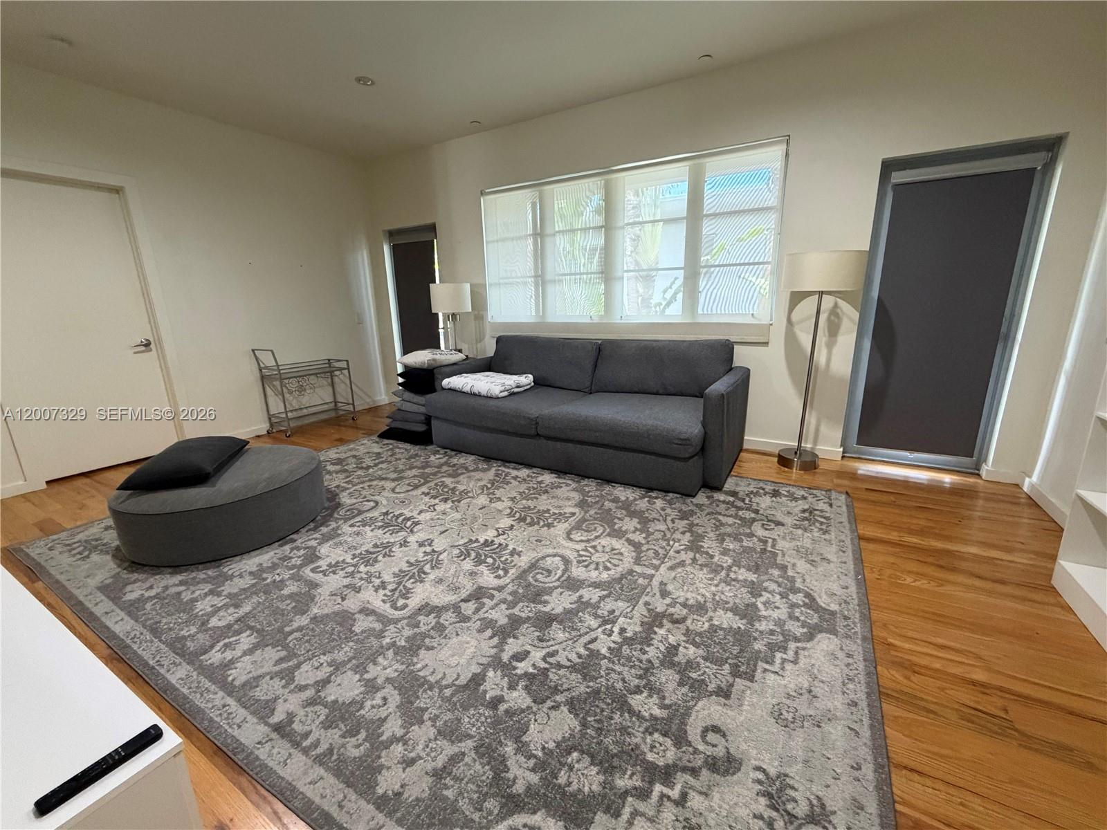 A living room features a gray sofa, a patterned area rug, and hardwood flooring — 1551 Lenox Ave # 7, Miami Beach FL 33139, MIAMI BEACH, FL