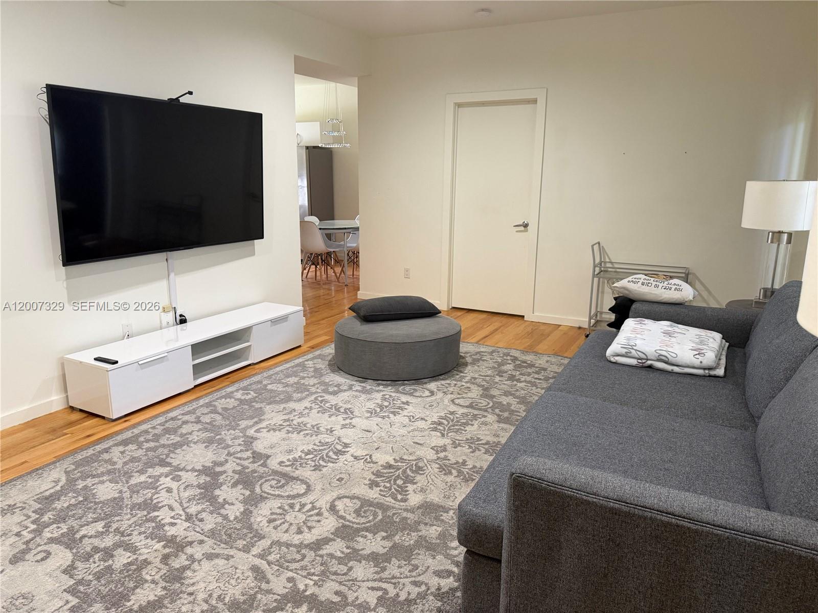 A living room features a wall-mounted television, a white media console, and a gray sofa — 1551 Lenox Ave # 7, Miami Beach FL 33139, MIAMI BEACH, FL