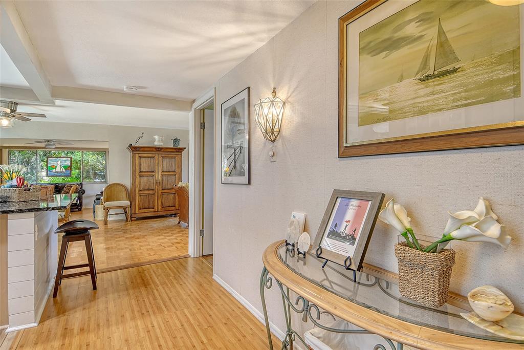 A hallway with light wood flooring leads into a living area with a wooden cabinet — 2308 WATERBLUFF PLACE UNIT V304, SARASOTA, FL
