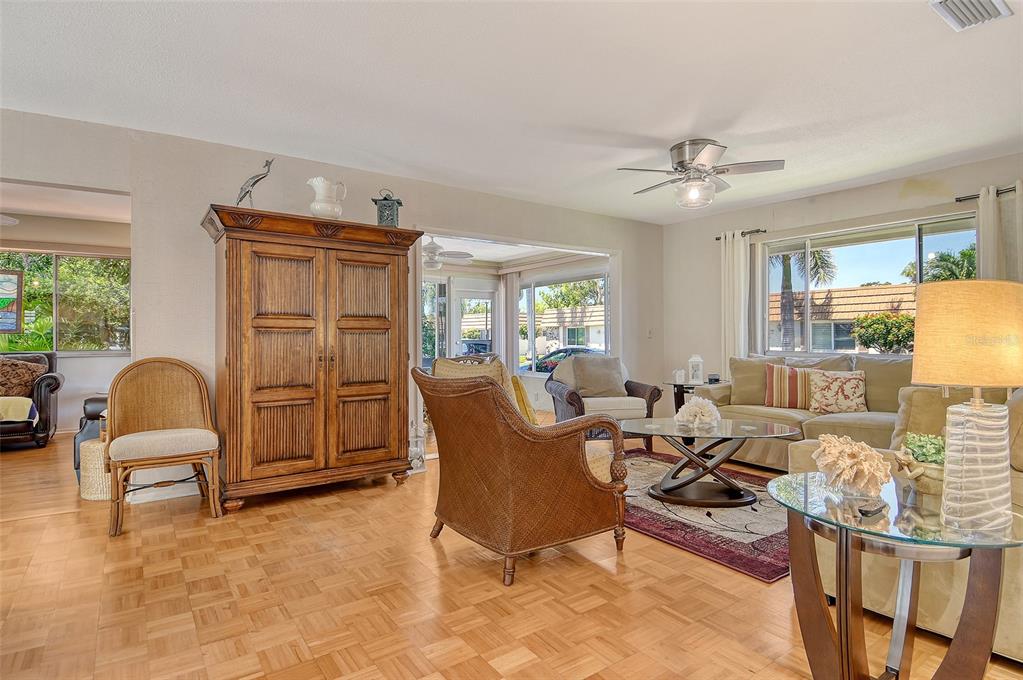 A living room with hardwood floors, wicker furniture, a large wooden armoire, and a ceiling fan — 2308 WATERBLUFF PLACE UNIT V304, SARASOTA, FL