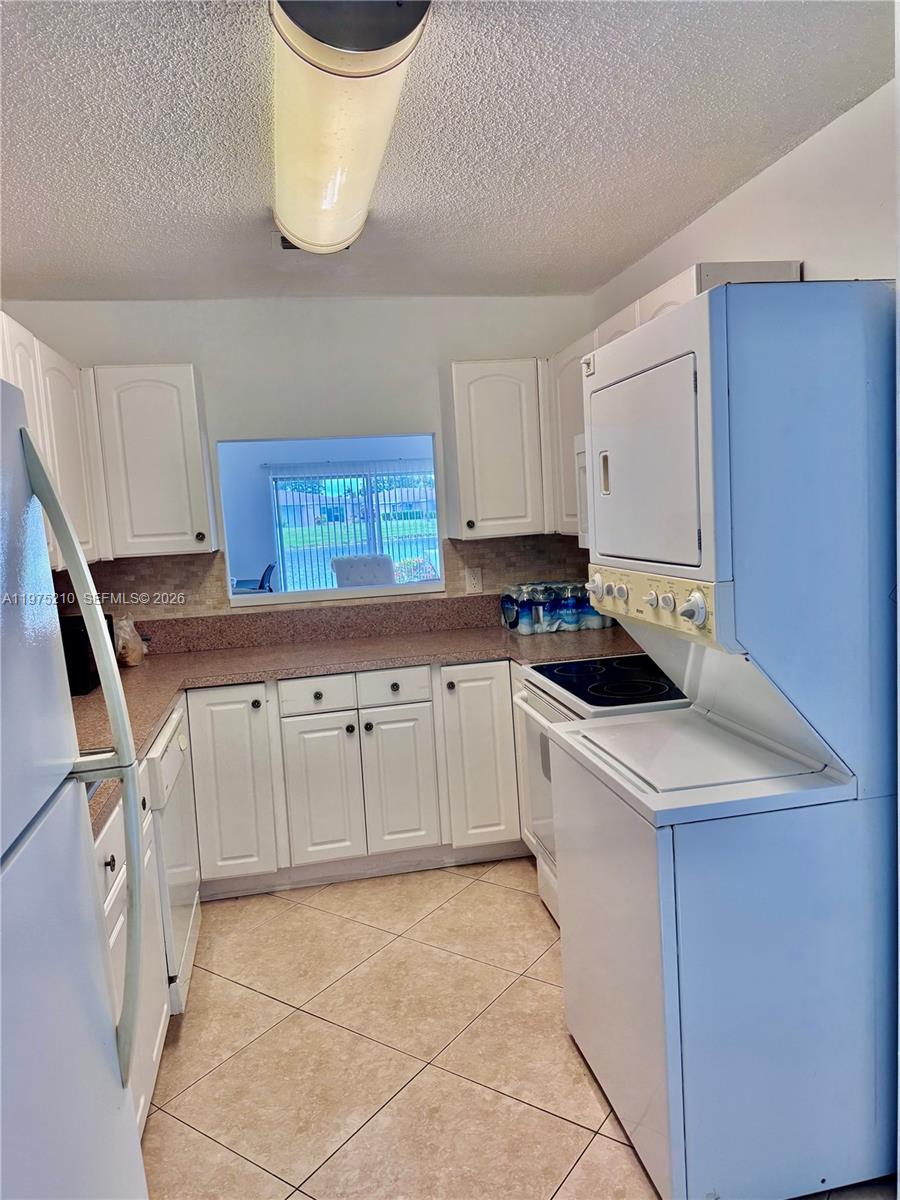 A kitchen features white cabinets, speckled countertops, tile flooring, and a stacked laundry unit — 8838 Bella Vista Dr, Boca Raton FL 33433, BOCA RATON, FL